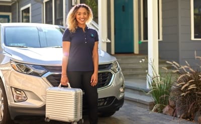 a woman stands in front of a car with a rolling suitcase